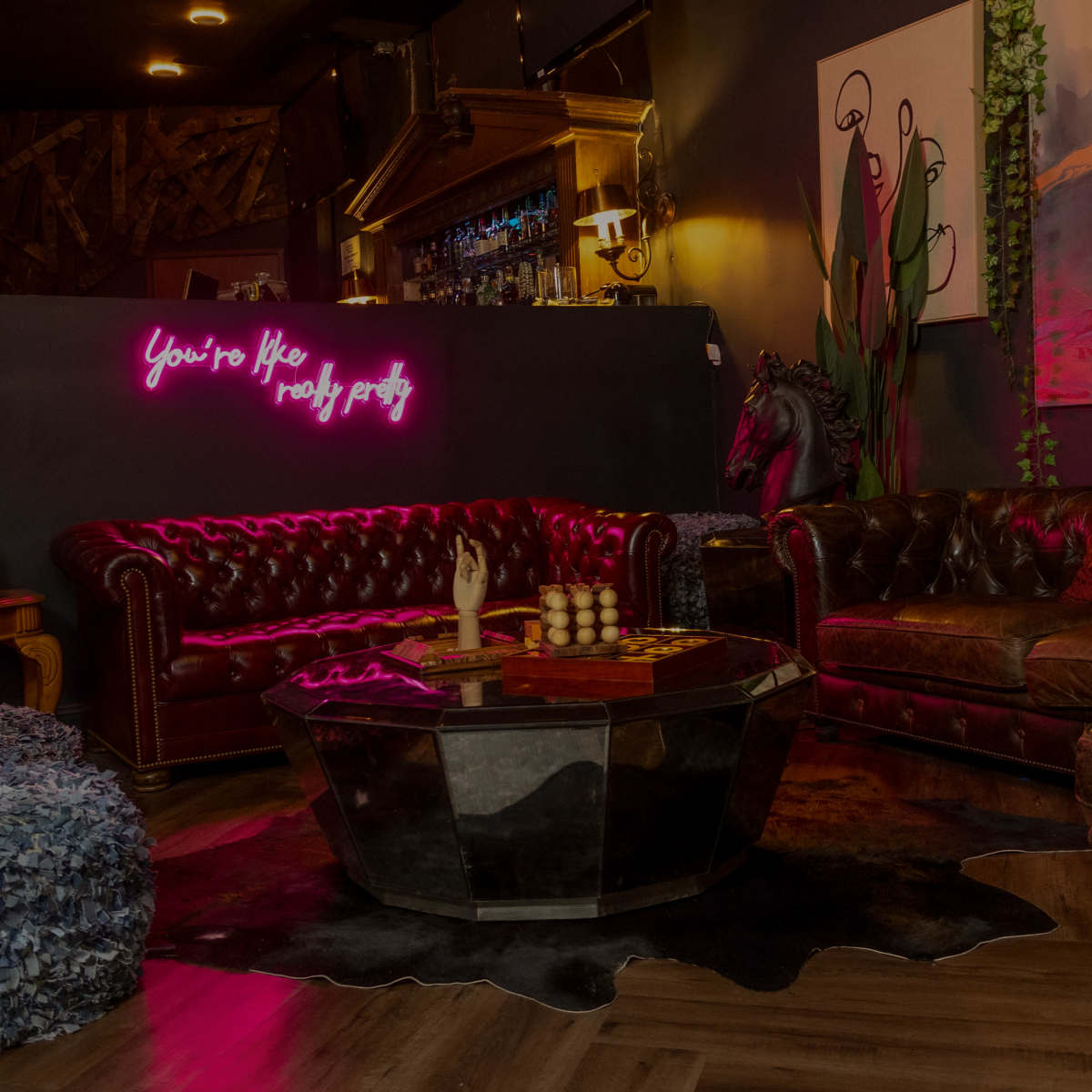 A cozy lounge area features a leather sofa, a wooden coffee table, and neon lighting on the wall.