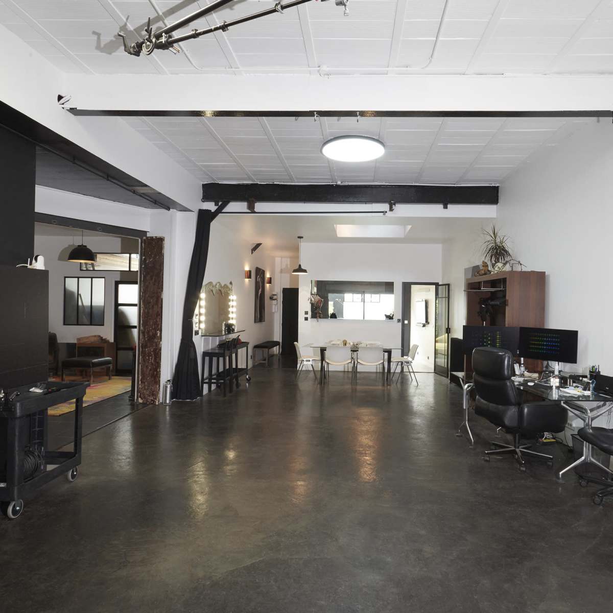 A spacious, modern studio with a polished concrete floor, black and white walls, and various furniture arrangements, including styling chairs and tables.