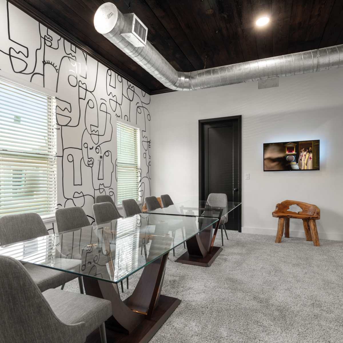 A modern conference room with a glass table, gray chairs, and a wall featuring abstract line art.