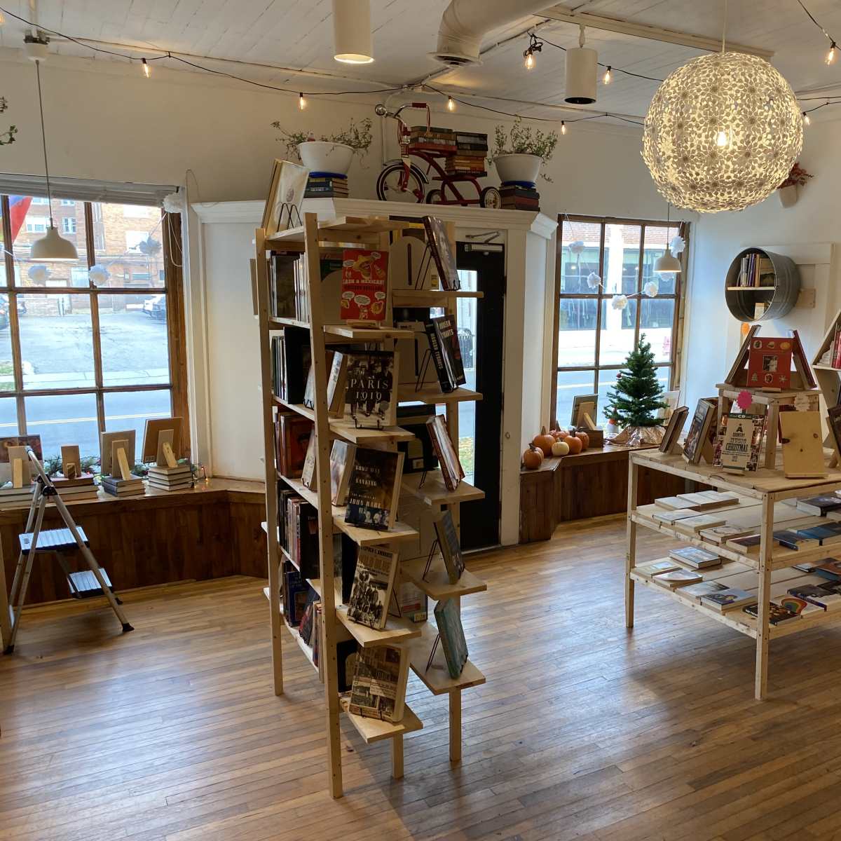 A cozy bookstore interior with bookshelves displaying various books, a central table with more books, and large windows allowing natural light to enter the space.