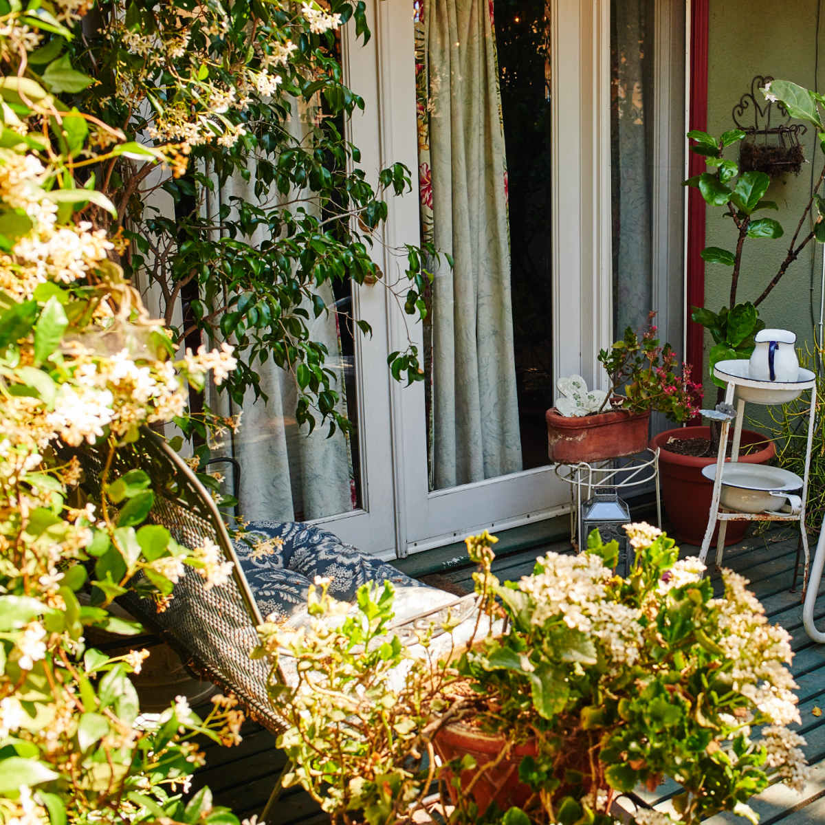 A white chair and a small side table are situated on a wooden deck surrounded by various potted plants.