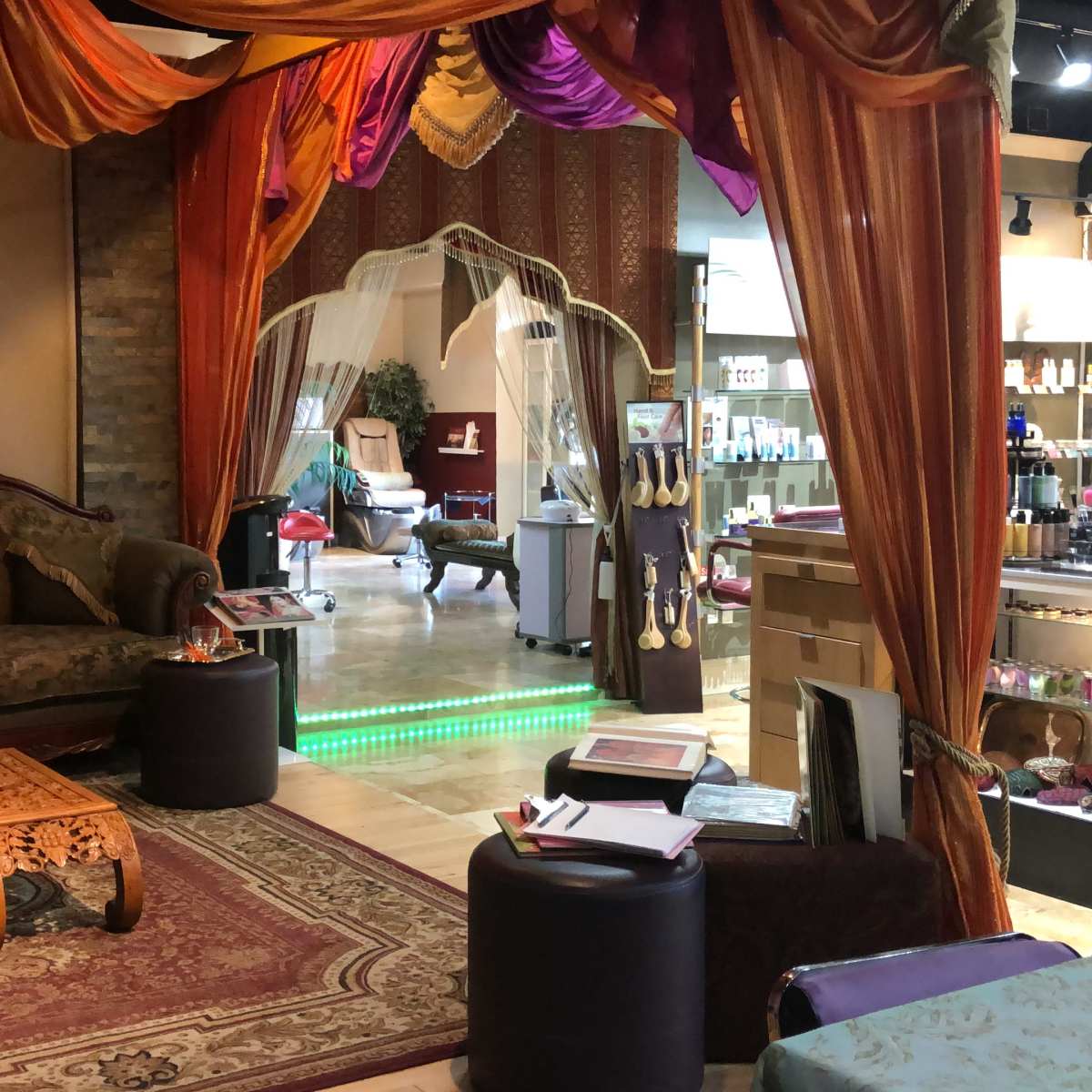 A cozy salon interior featuring ornate seating, decorative drapes, and a reception area with beauty products displayed on shelves.
