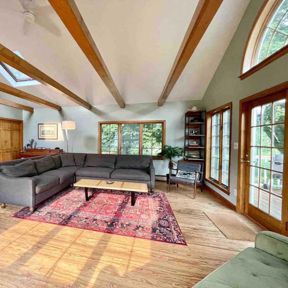 A spacious living room features a gray sectional sofa, a coffee table on a patterned rug, and large windows providing natural light.
