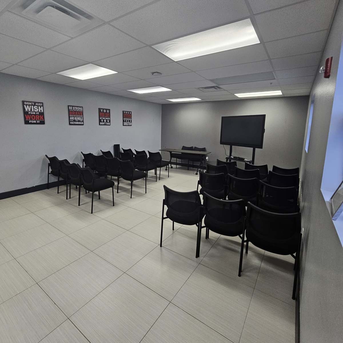 A spacious meeting room with rows of black chairs facing a television and a few motivational posters on the walls.