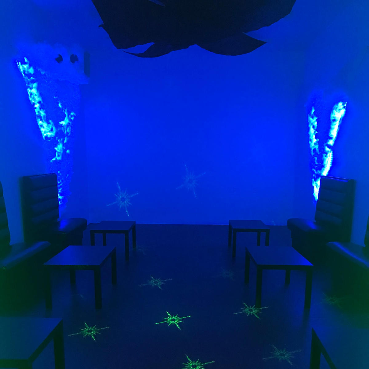A dimly lit room with blue and green lighting, featuring black chairs and tables arranged in a symmetrical layout.