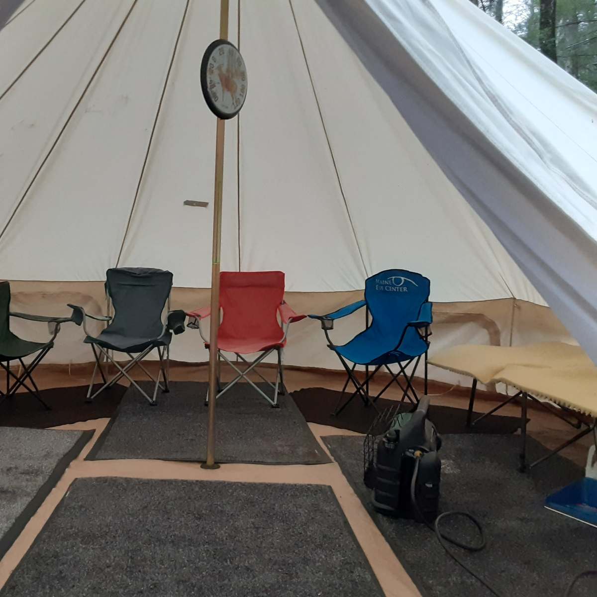 The interior of a large tent featuring four folding chairs arranged around a central pole on a carpeted floor.