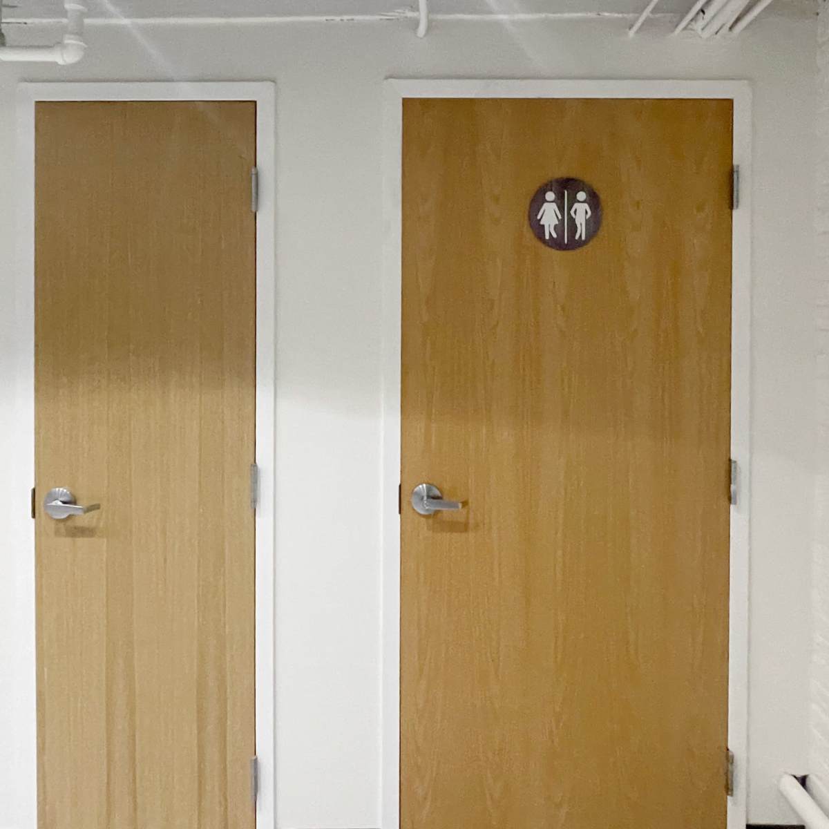 Two wooden doors labeled for gendered restrooms, located in a modern interior corridor.
