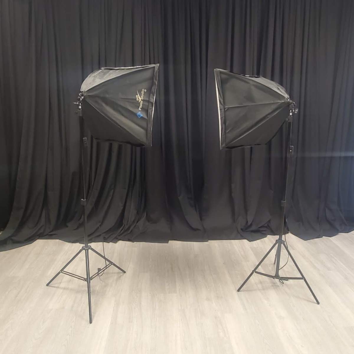 Two softbox lights on adjustable stands facing each other against a backdrop of black fabric.