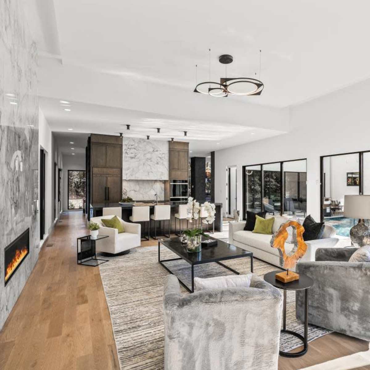 A modern open-concept living area with a marble accent wall, stylish furniture, and large windows overlooking a pool.