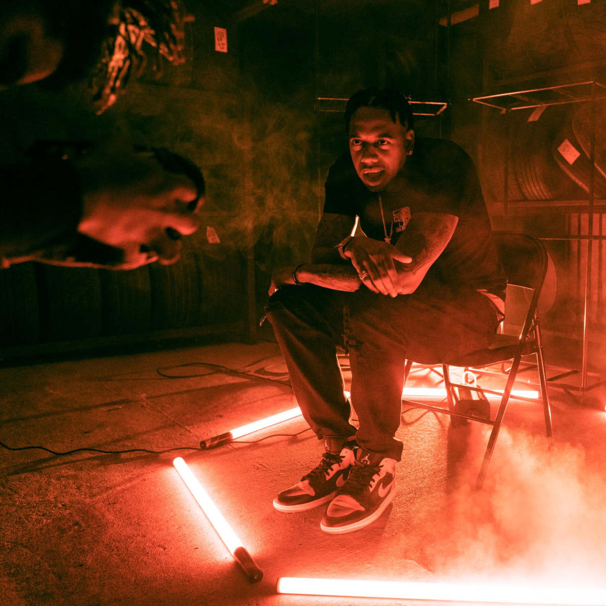 A person sits in a chair surrounded by glowing neon lights and mist in a dimly lit indoor space.