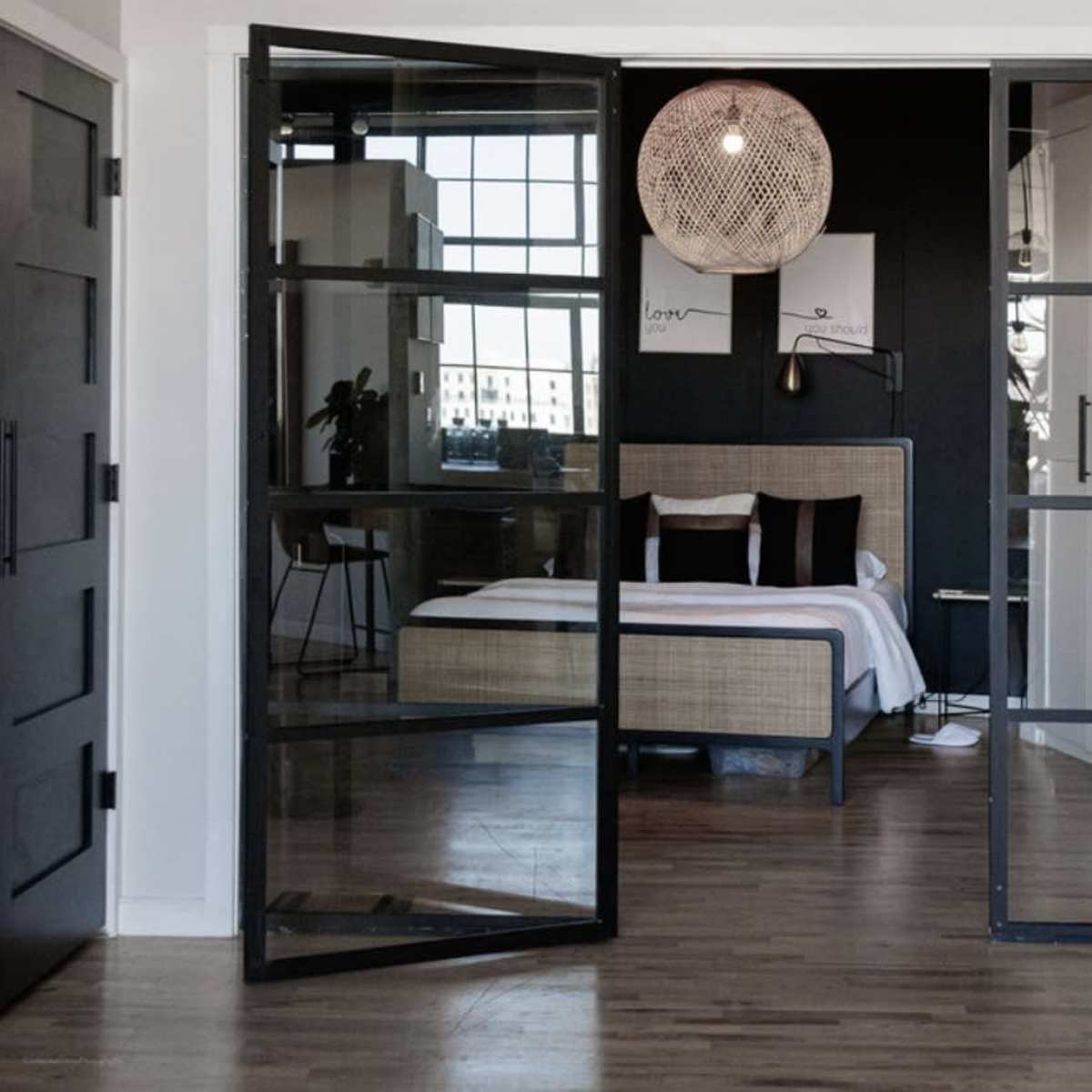 A modern bedroom with a queen-sized bed is visible through large glass doors in a stylish interior.