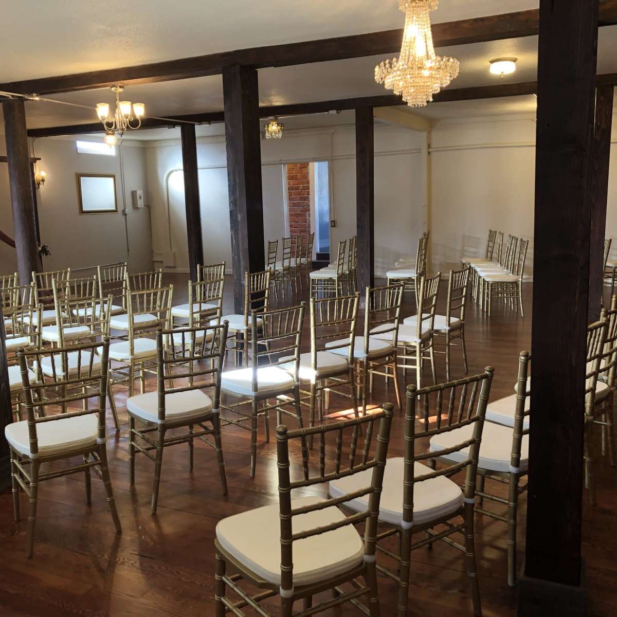 An empty event space features rows of gold chiavari chairs arranged on a polished wooden floor beneath chandeliers.