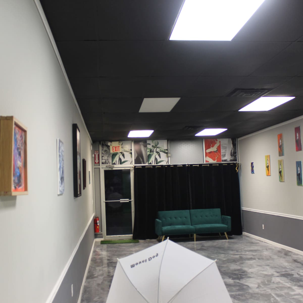 A well-lit art gallery with a green couch, colorful artwork on the walls, and a curtain at the back.