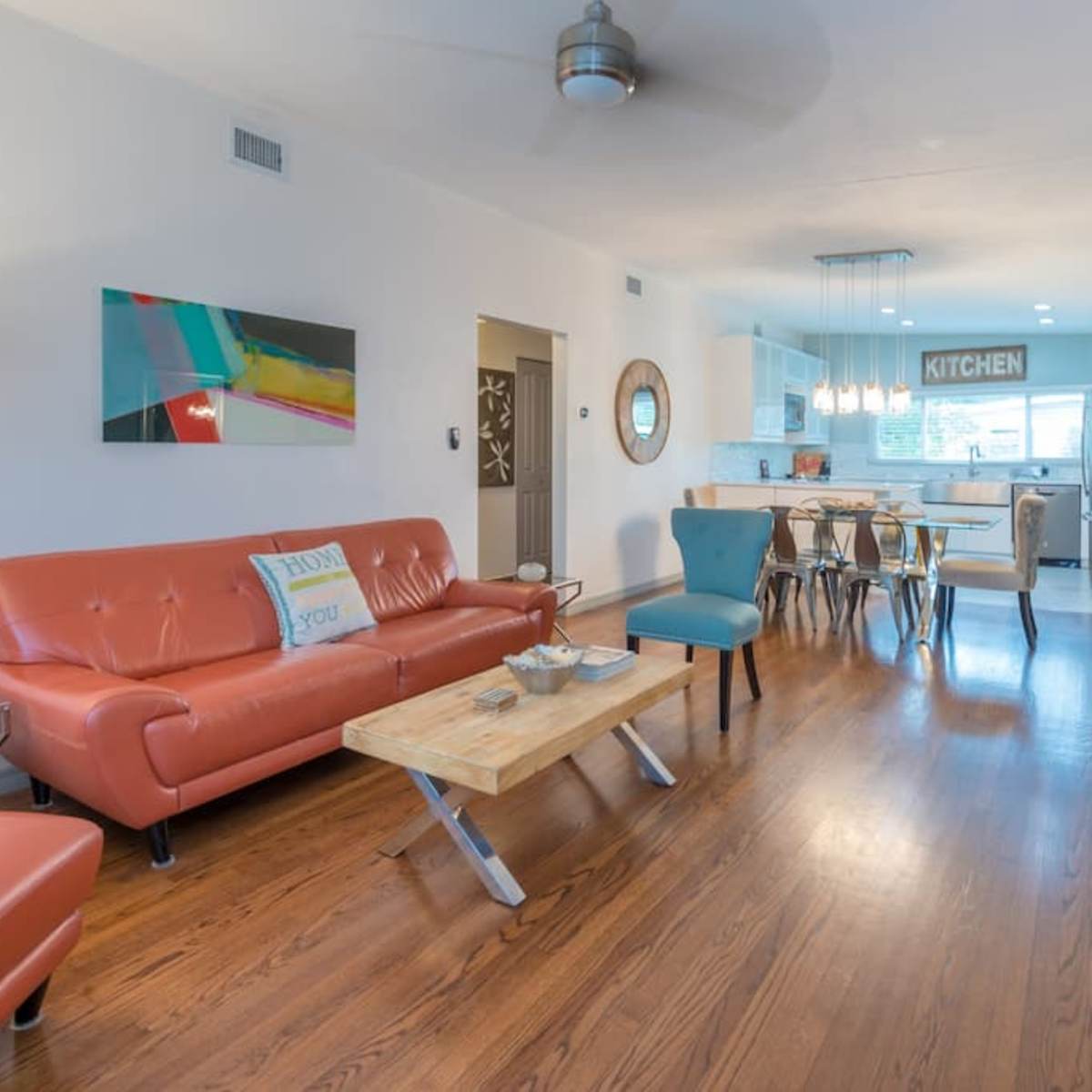 A modern living room with an orange sofa, wooden tables, and an open kitchen in the background.