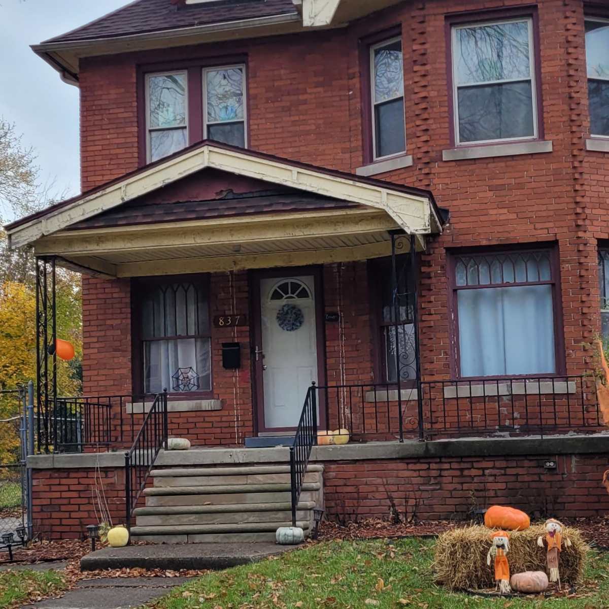 A two-story red brick house features a front porch and decorative pumpkins in the yard.