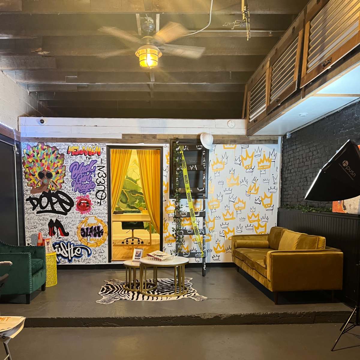 A creatively decorated interior space with colorful graffiti on the walls, a yellow curtain framing a doorway, a green artwork visible inside, and a brown sofa in the foreground.