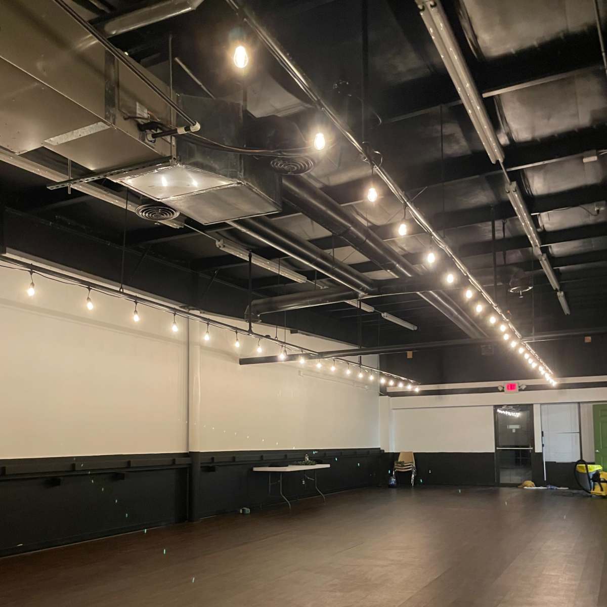 A spacious, empty room with dark flooring, white walls, and overhead lights.