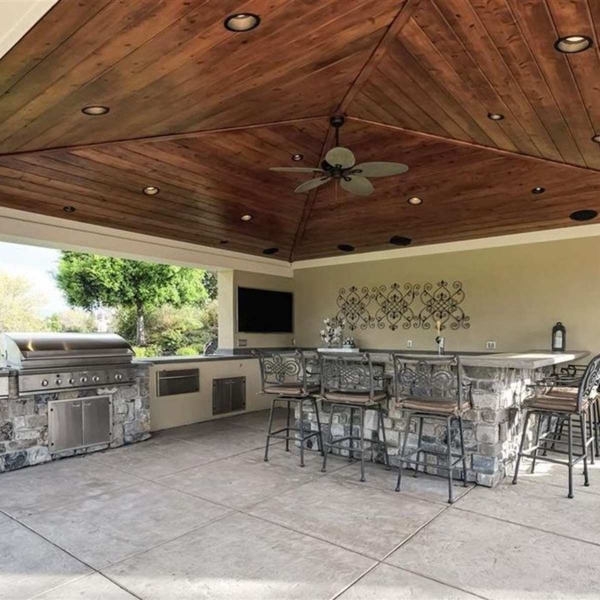 An outdoor kitchen and dining area with a stone grill, bar seating, and a wooden ceiling.