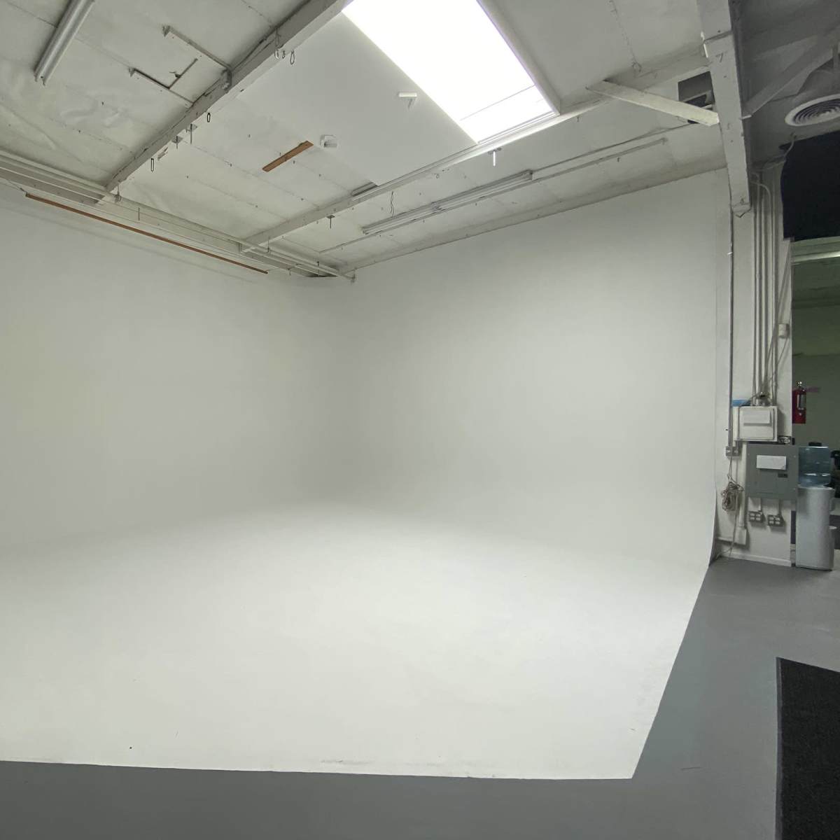 A spacious, empty photo studio with a white backdrop and gray flooring.