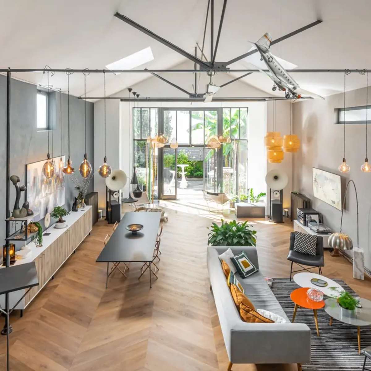 A modern open-plan living space with a dining area, a lounge, and large windows that lead to an outdoor patio, featuring wooden flooring and contemporary furnishings.