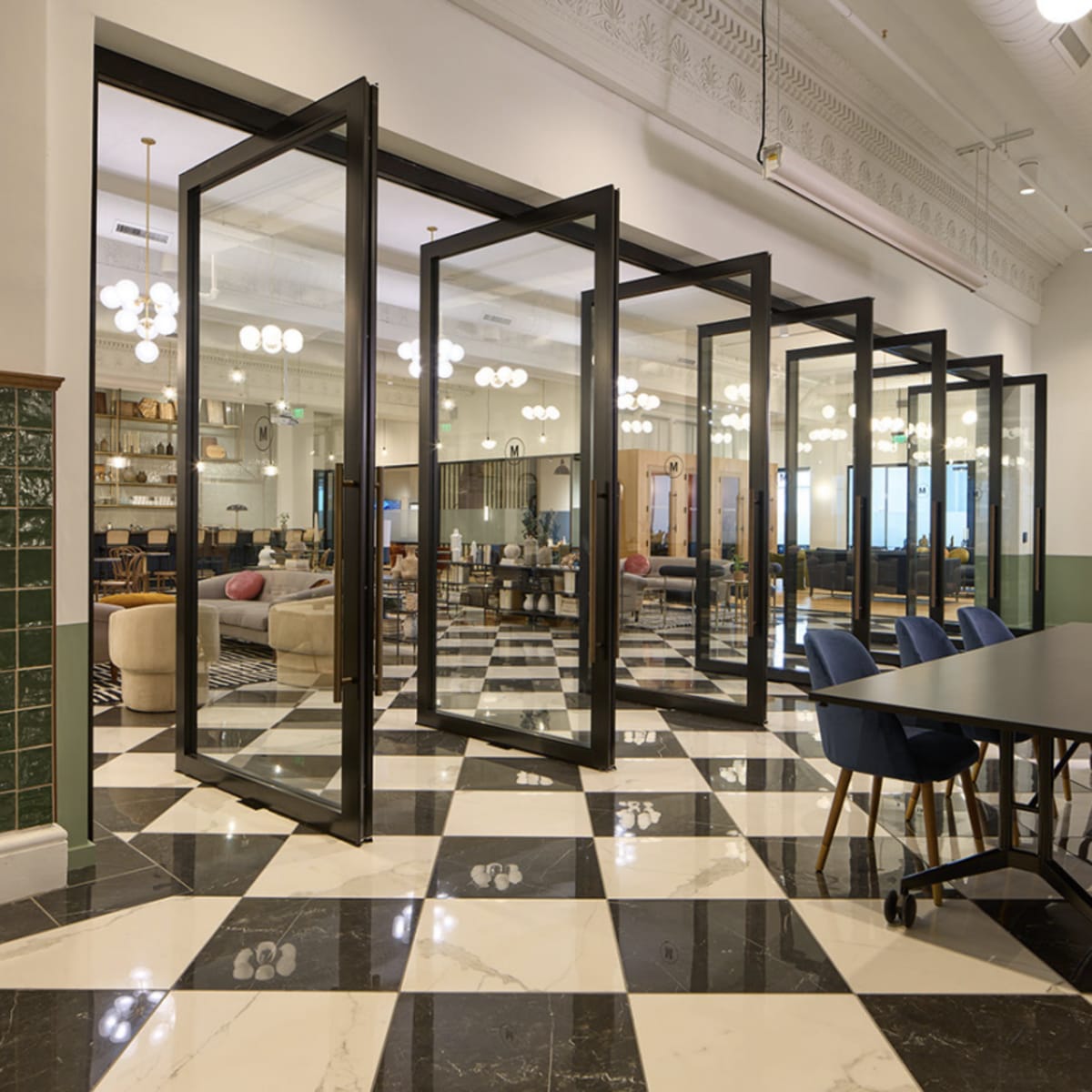 A modern office space with large glass doors separating multiple meeting rooms, featuring a checkered black and white floor.
