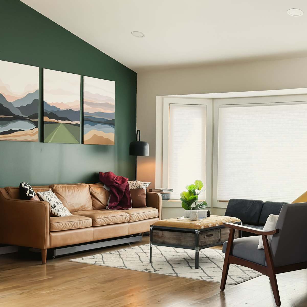 A modern living room featuring a leather sofa, a gray sofa, a coffee table, and artwork on the walls, with large windows allowing natural light to enter.