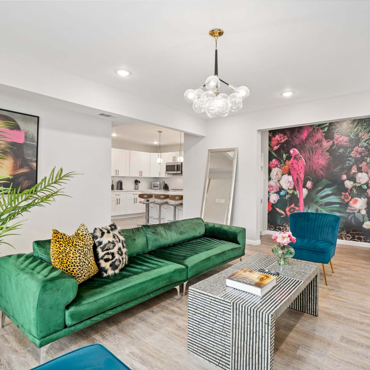 The living room features a green velvet sofa, a striped coffee table, and a floral mural on one wall, complemented by modern furnishings.
