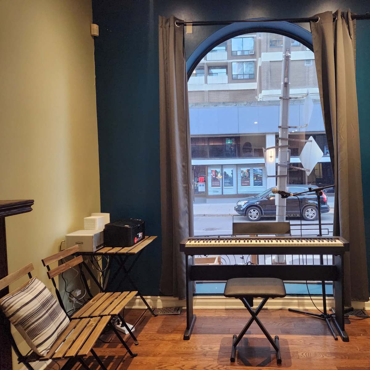 The scene shows a small room with a keyboard, a chair, and a speaker next to a large window overlooking a street.