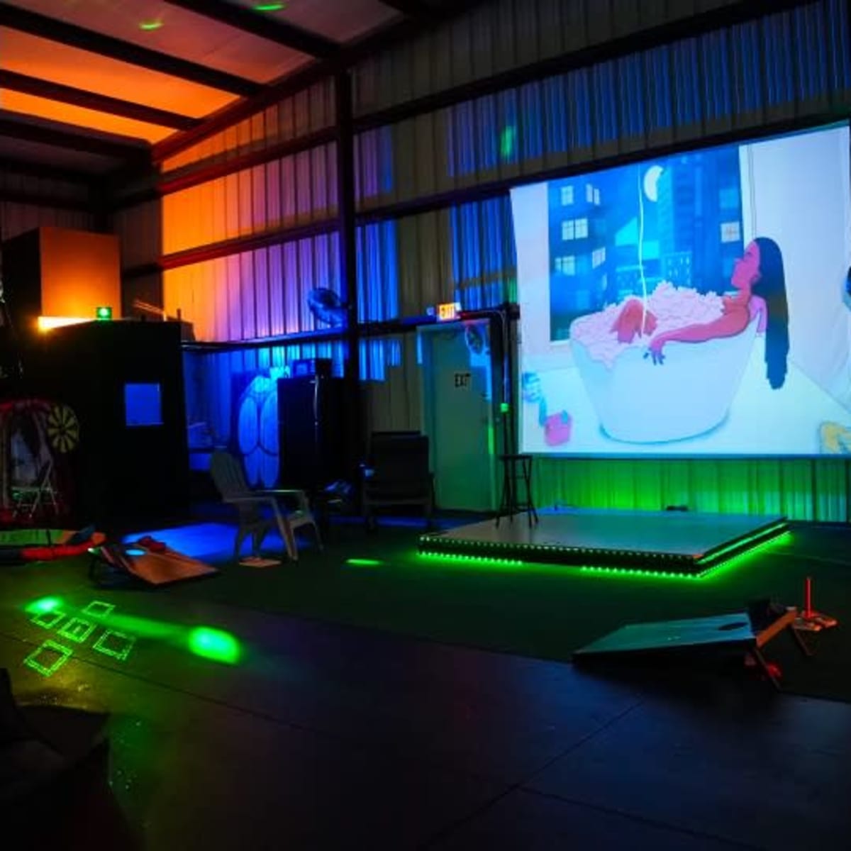 A large projection screen displays an animated scene of a figure in a bathtub, surrounded by colorful lighting in a spacious indoor area.