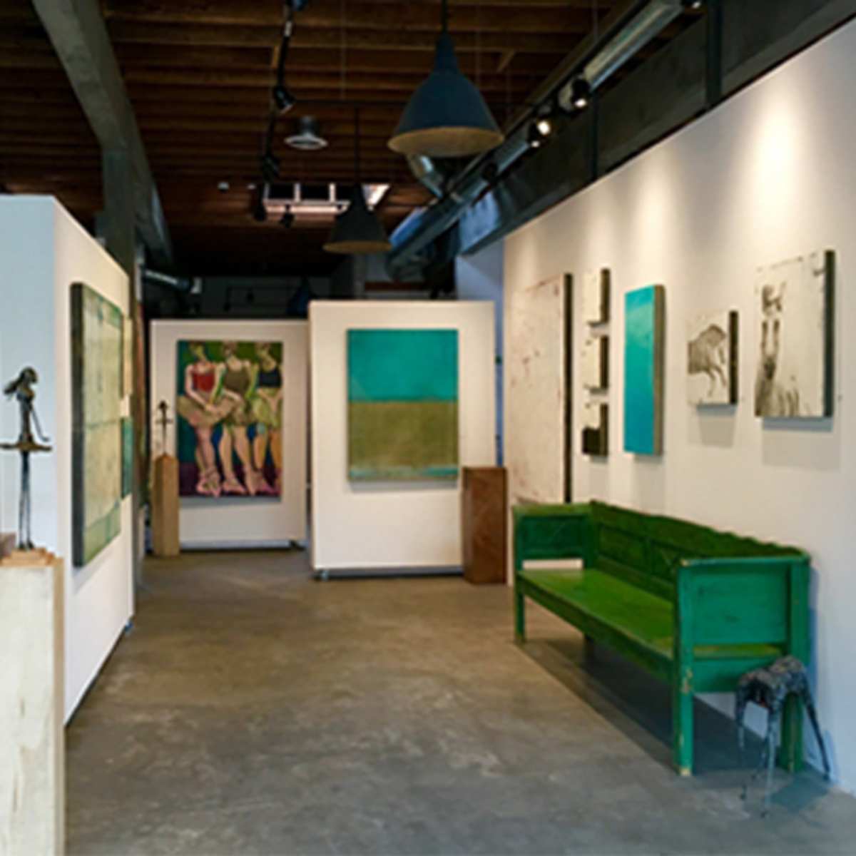 An art gallery interior featuring various colorful abstract paintings on the walls, with a green bench and seating area in the center.