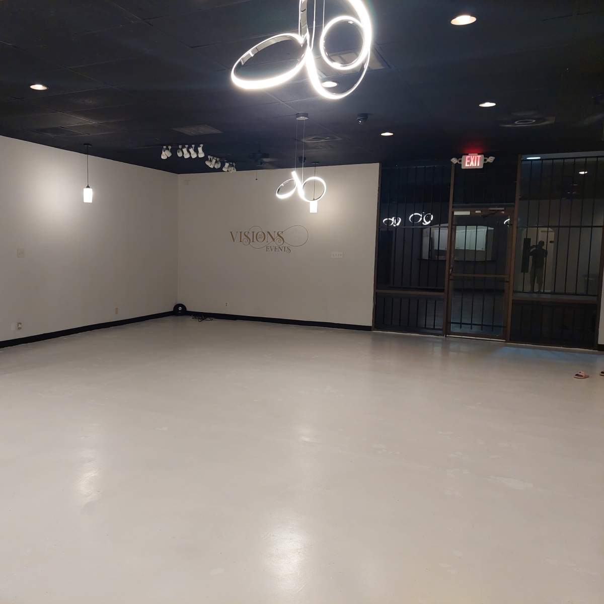 An empty, well-lit room with white walls and a polished floor, featuring several hanging light fixtures.