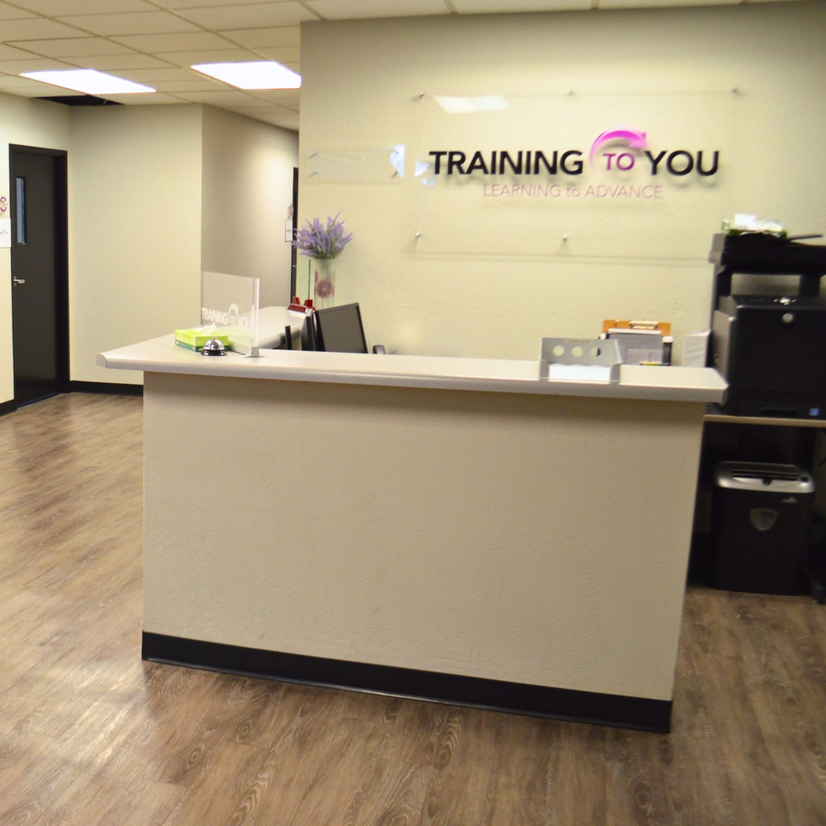 A modern office reception area with a front desk, a small kitchenette, and a door leading to another room.