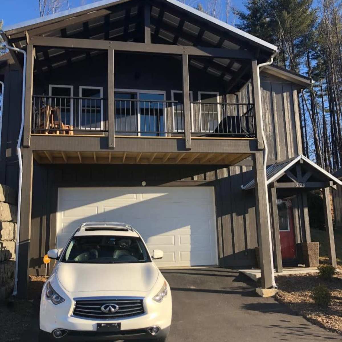A two-story house with a balcony, featuring a white car parked in front of it and a garage door beneath the balcony.