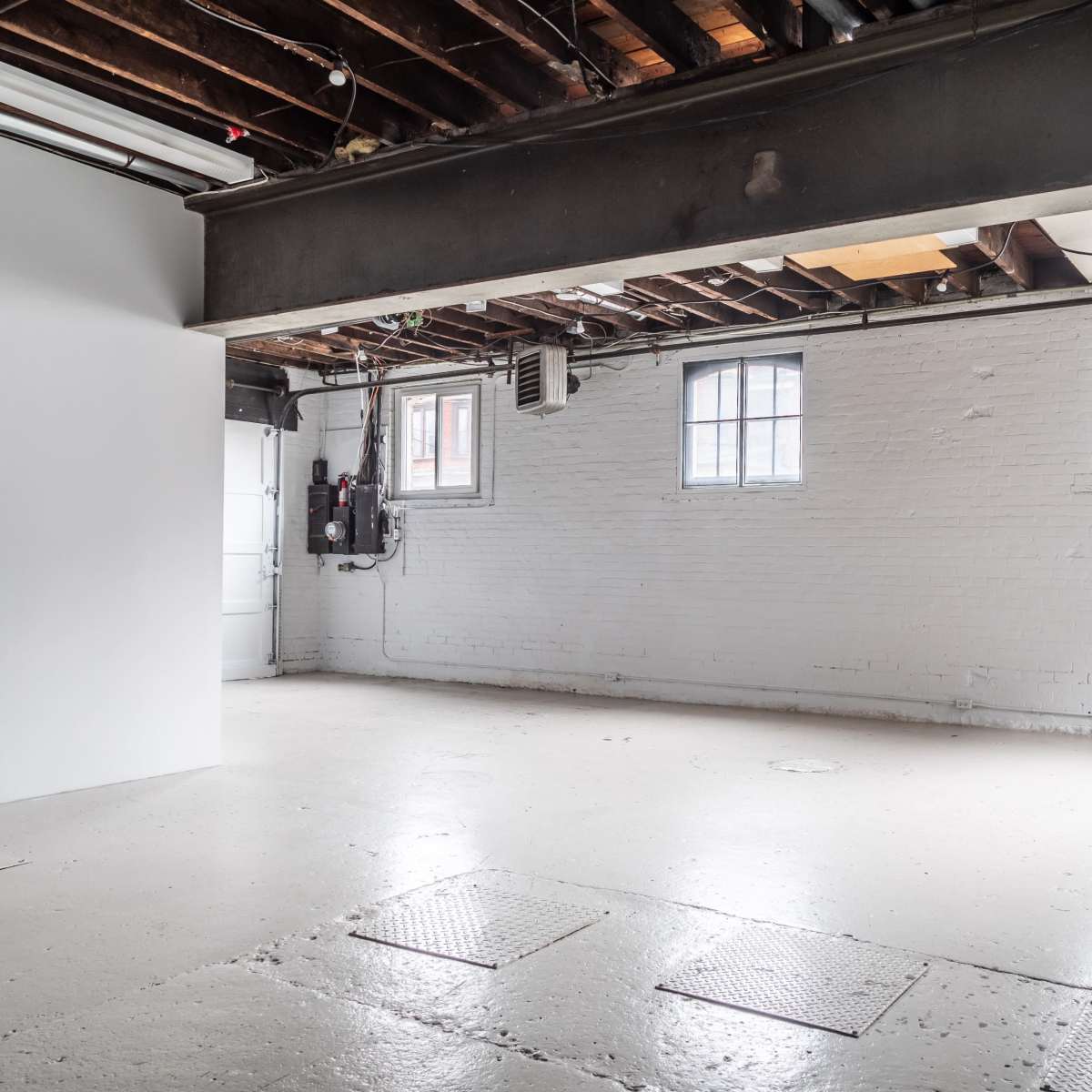 An empty room with exposed beams, three windows, and a concrete floor.