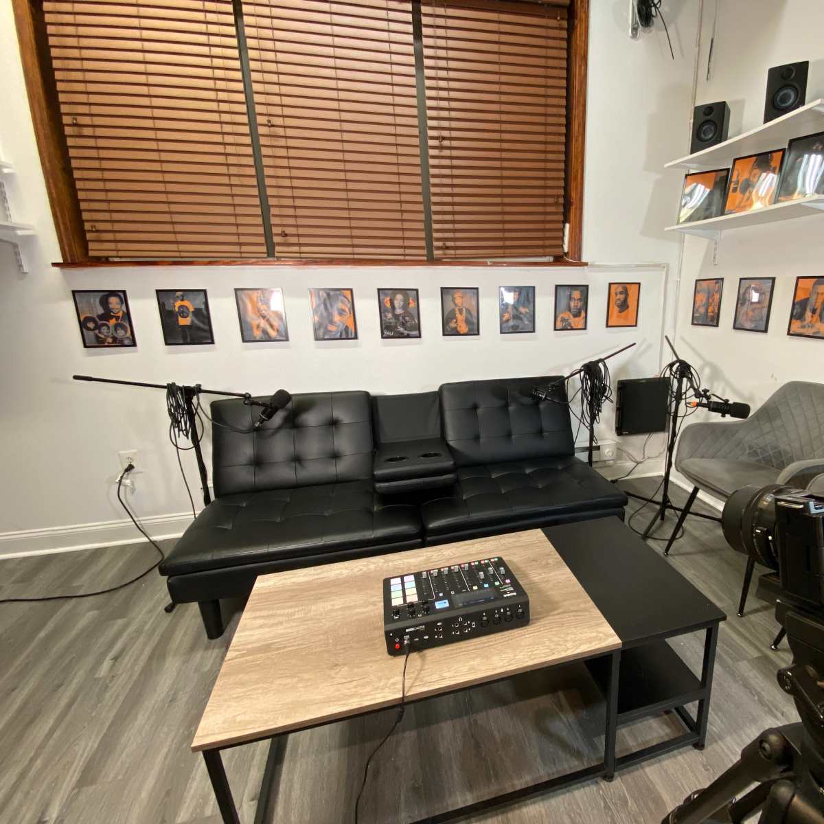 A recording studio with a black couch, a coffee table, two microphones set up, and framed artwork on the walls.