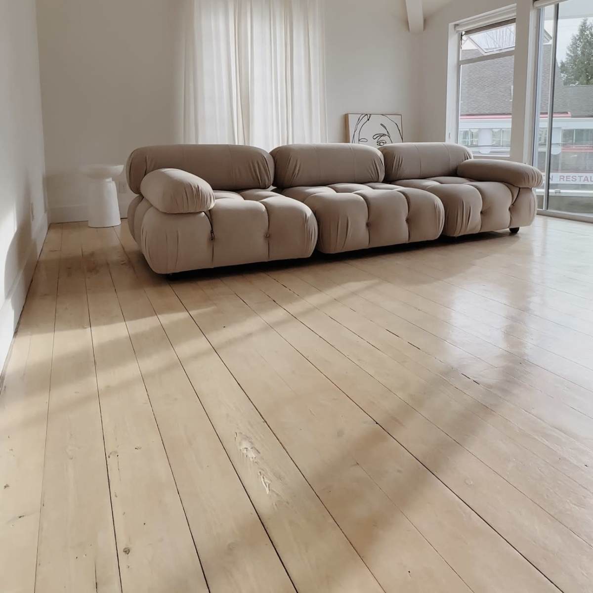 A spacious living room featuring a large, light-colored sofa and a large window with sheer curtains.