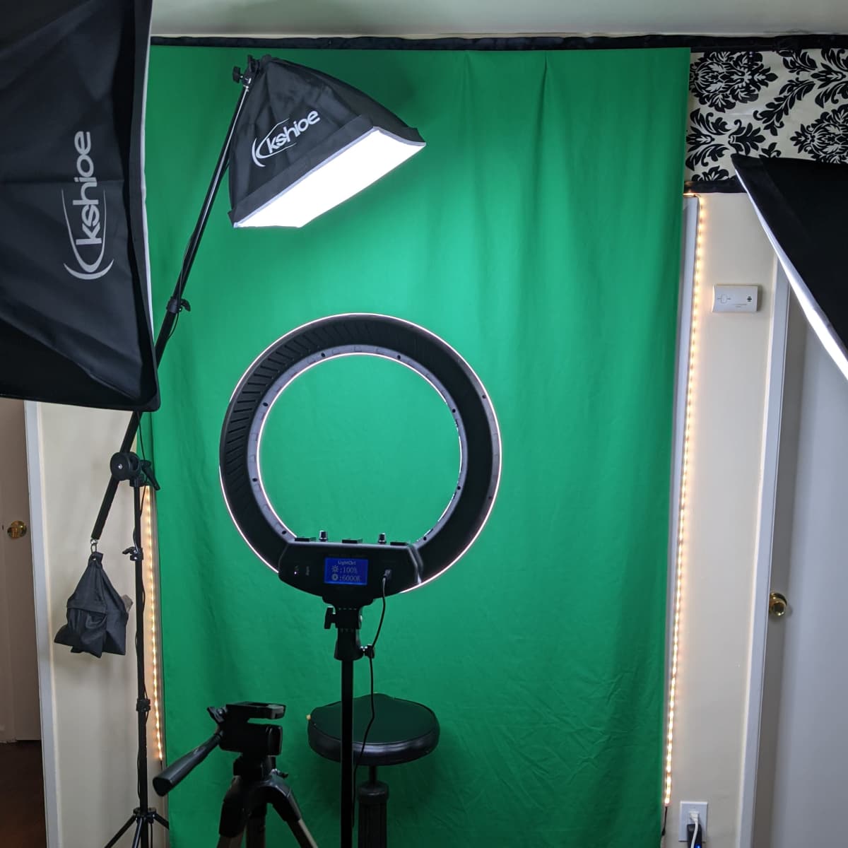 A photography setup with a green backdrop, a ring light, and a stool positioned in front of a camera on a tripod.