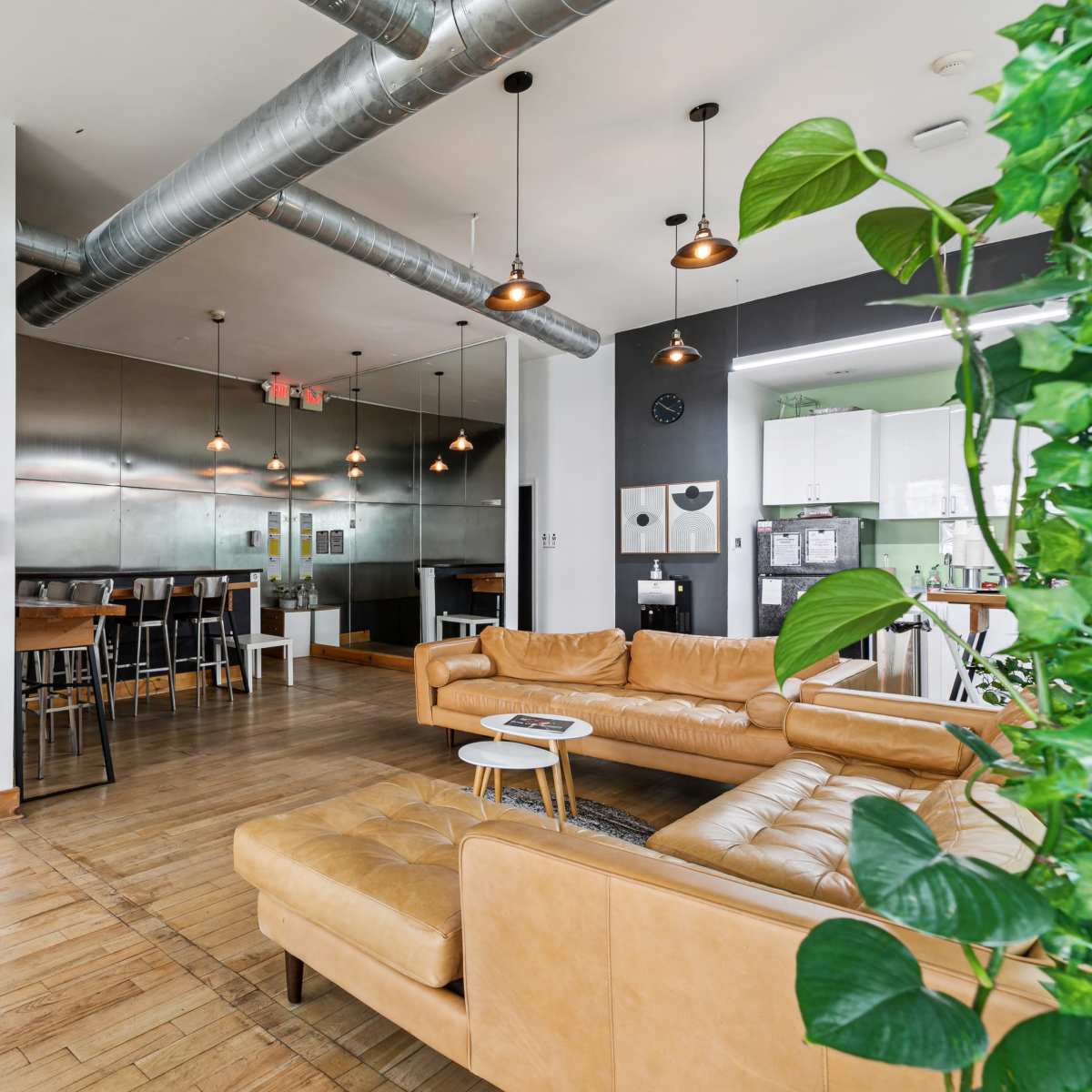 A modern open-concept living space featuring a leather couch, a dining area, and a kitchen with metallic finishes.