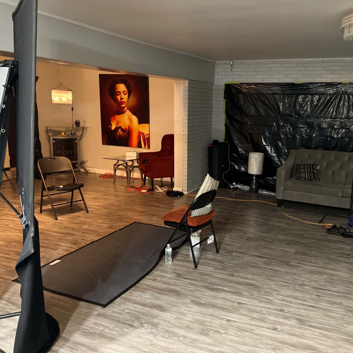A spacious room features a couch, several chairs, and a large artwork on the wall, with the area partly covered by black plastic sheets.