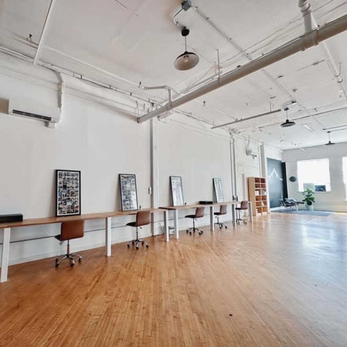 A spacious interior of an office with a long table and several chairs, framed pictures on the wall, and ample natural light coming from large windows.