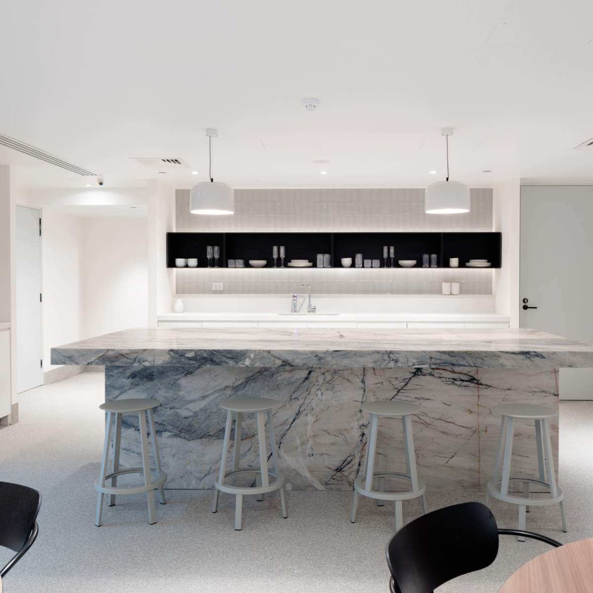 A modern kitchen features a large marble island with bar stools and sleek cabinetry, complemented by minimalist lighting and decor.