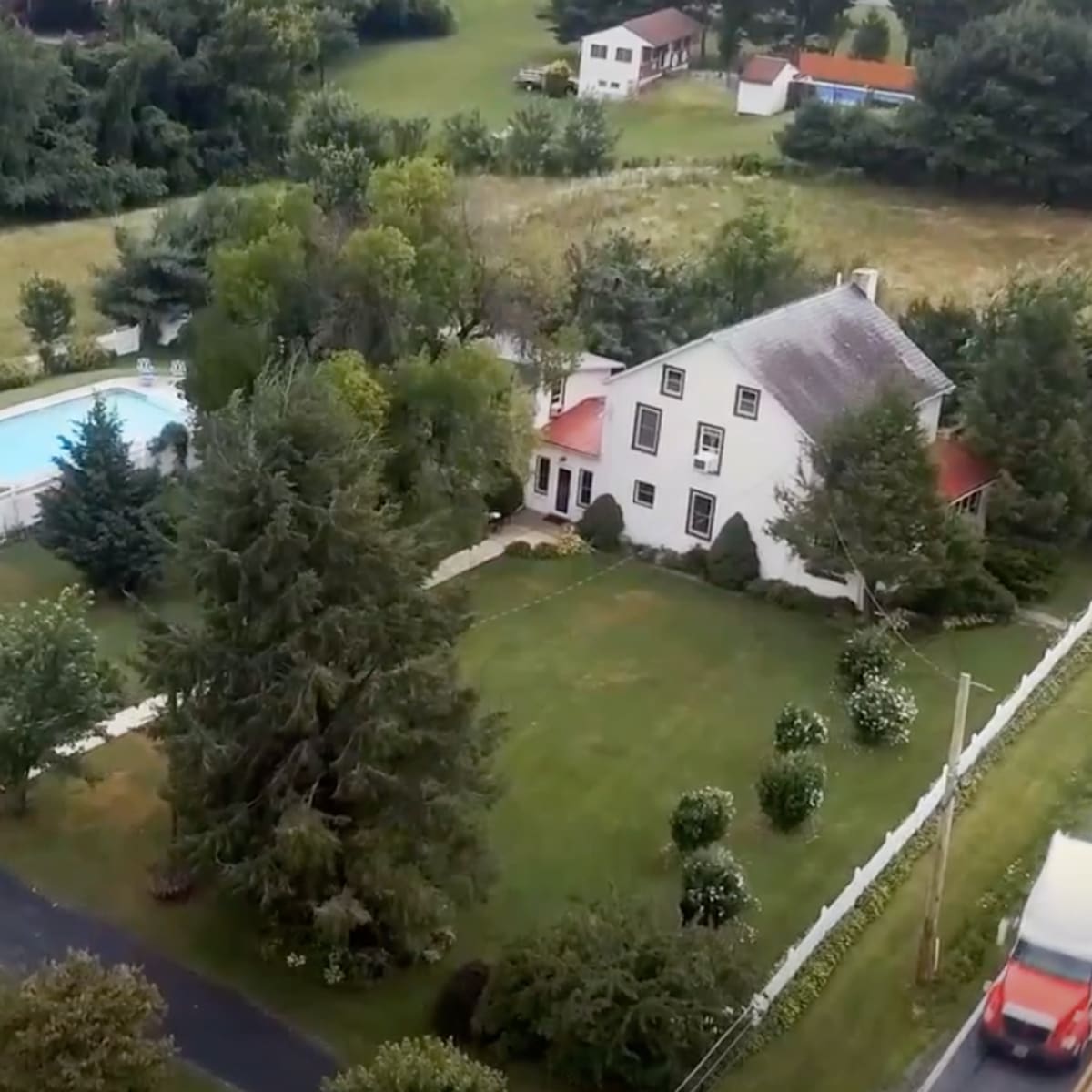 An aerial view of a rural property featuring a house, a swimming pool, several outbuildings, and landscaped grounds.