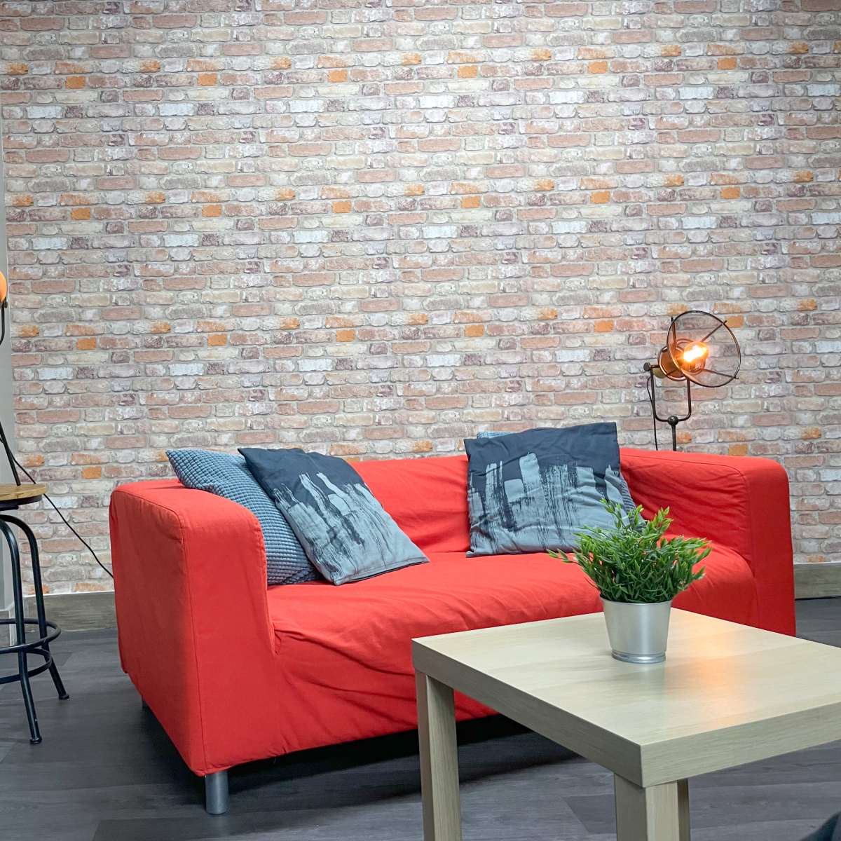 A modern living room with a red sofa, a small wooden table, and a vintage movie poster on the wall, set against a brick-patterned background.