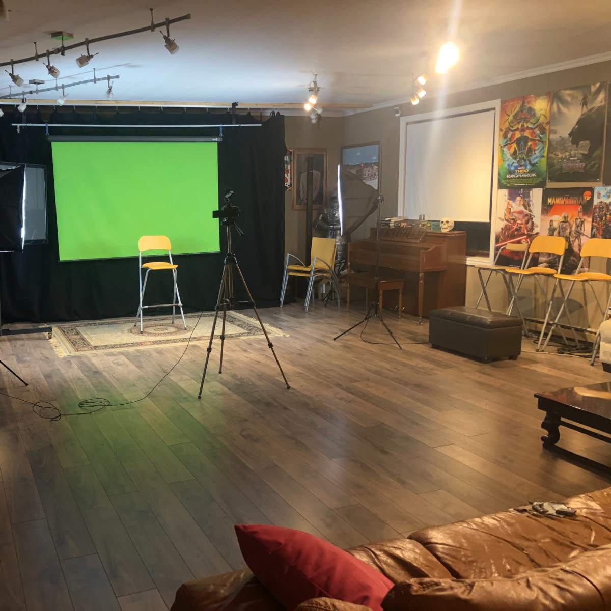 The room features a green screen setup with several chairs arranged around a camera and lighting equipment.