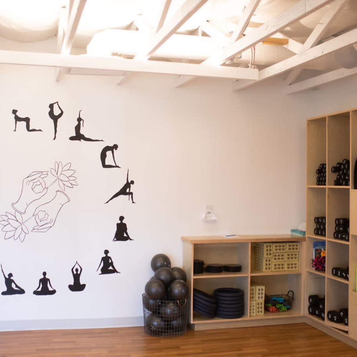 A yoga studio with a wall mural depicting various yoga poses and a shelf stocked with fitness equipment.