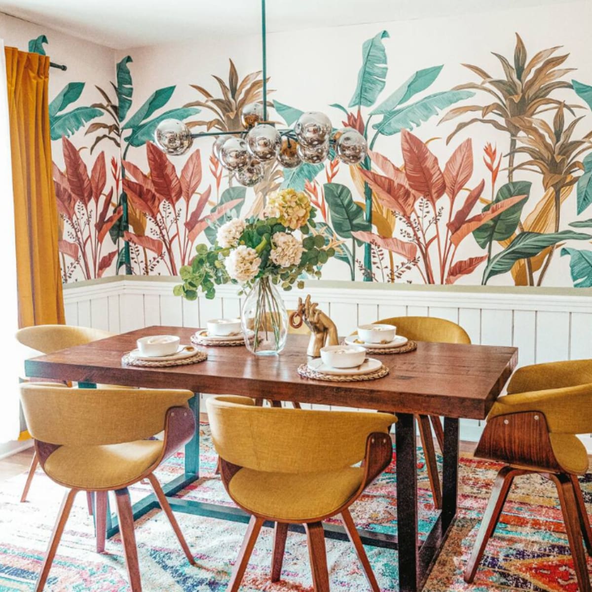The dining area features a wooden table with six chairs, surrounded by a vibrant plant-themed wallpaper and adorned with a floral centerpiece.