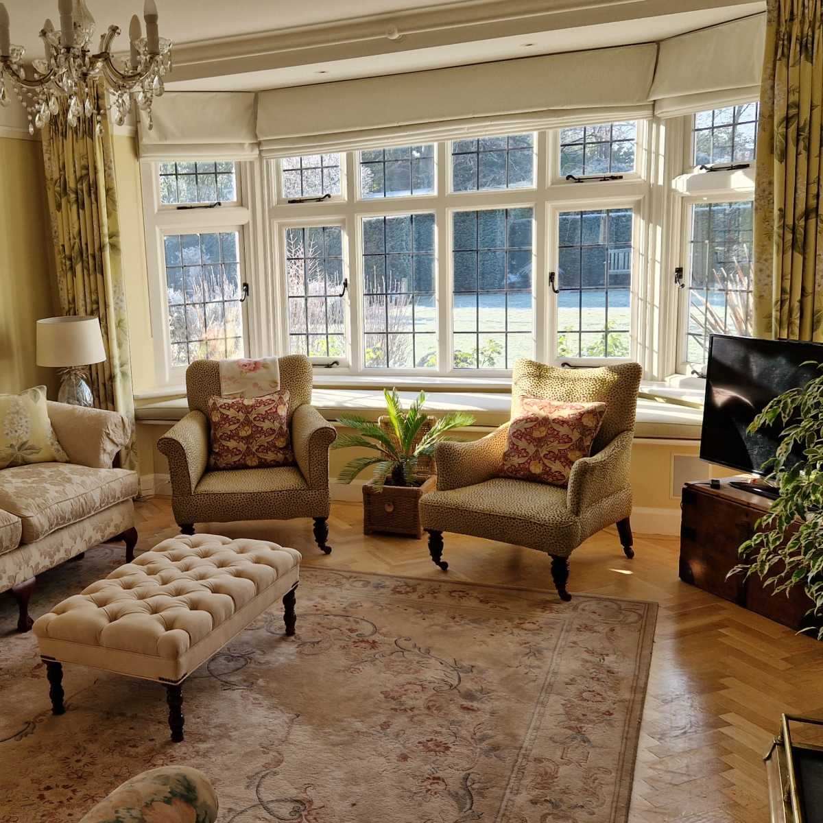 A well-furnished living room with a sofa, two armchairs, a decorative coffee table, and large windows letting in natural light.