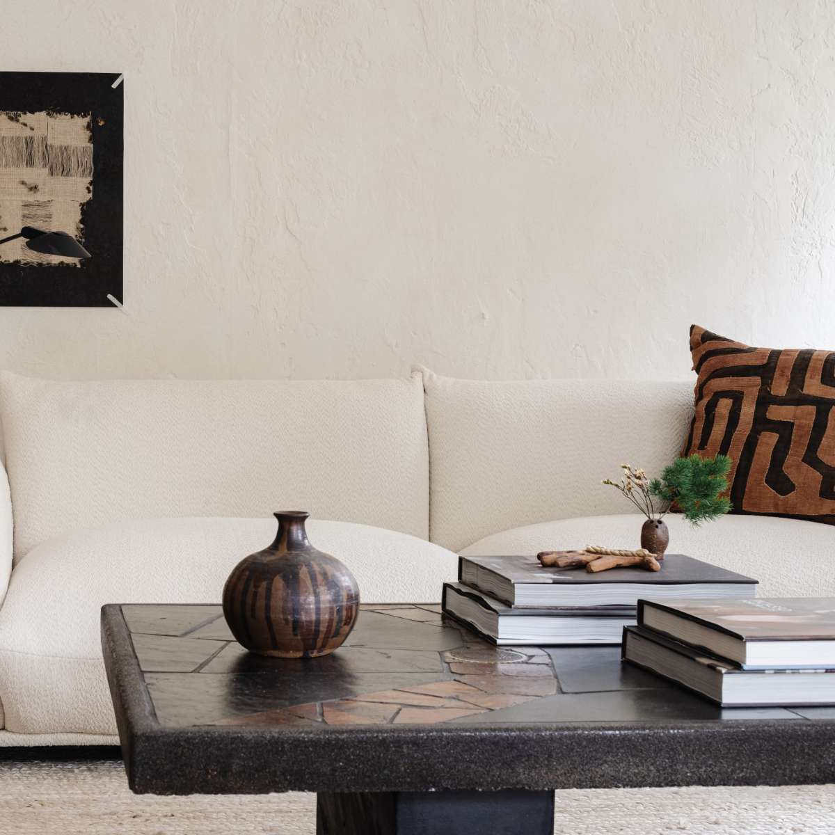 A minimalist living room featuring a white, curved sofa, a dark stone coffee table with stacked books, and a small decorative vase.