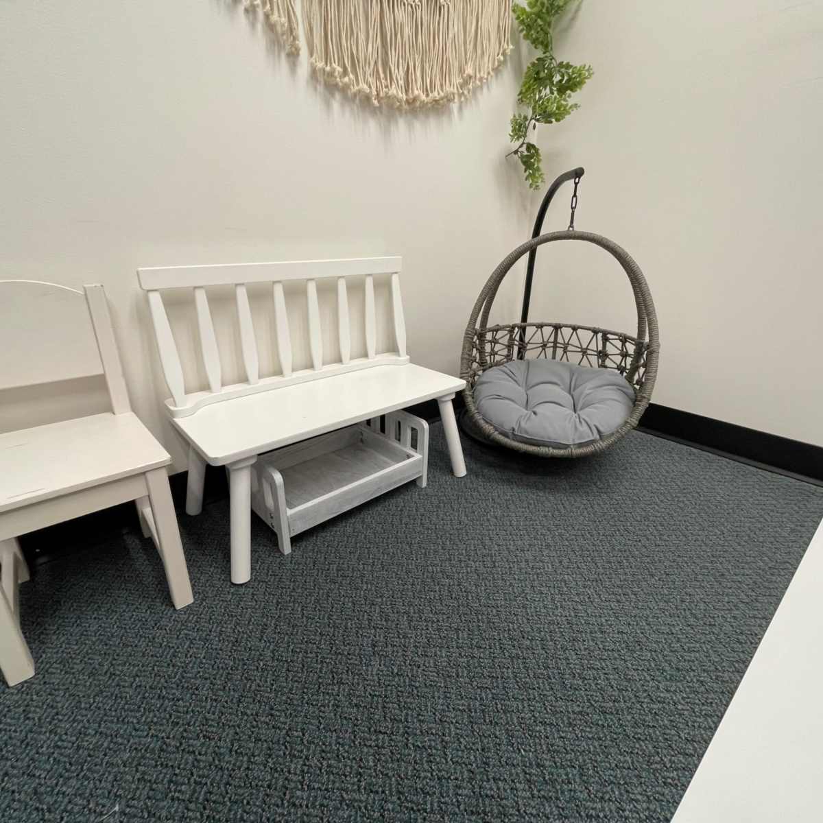 A small indoor area with a white bench, a single white chair, and a hanging, cushioned swing in a gray and green color scheme.
