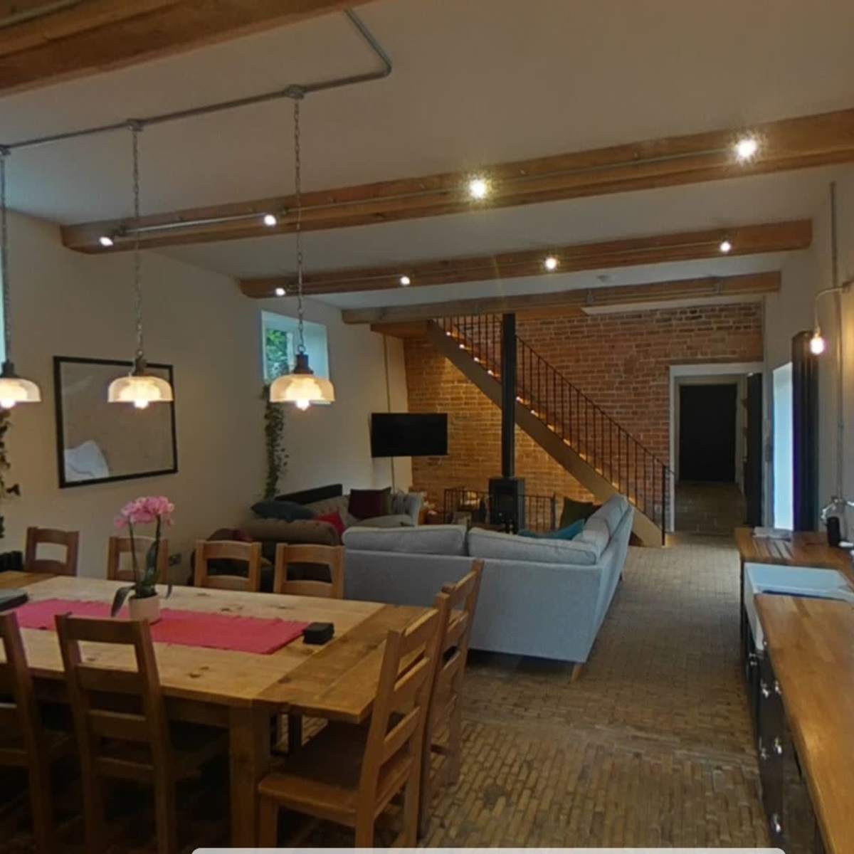 A modern interior space featuring a dining area with a wooden table and chairs, a living area with a sofa and television, and a staircase made of wood.